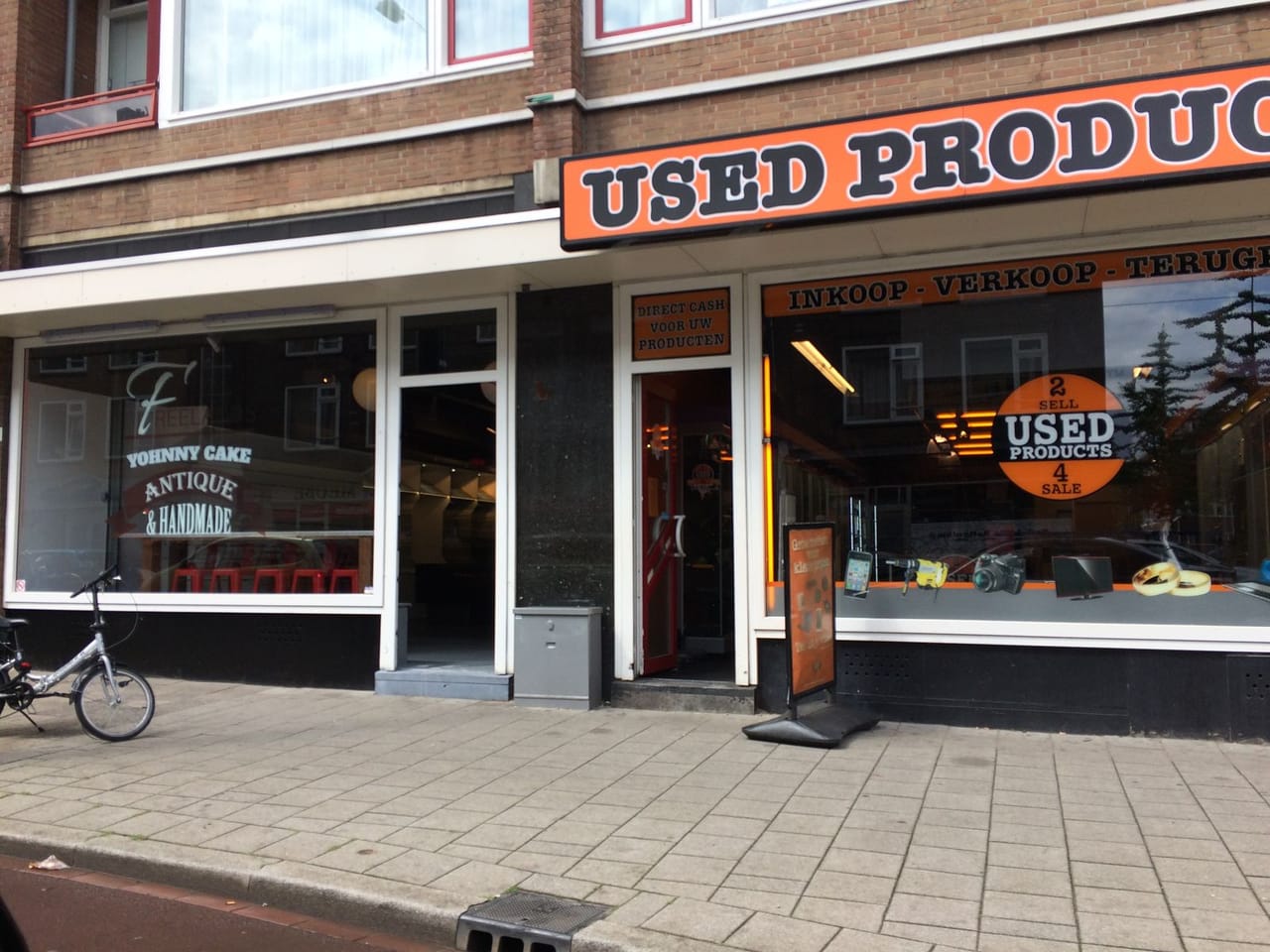 Yohnny Cake en buurpand Used Products, twee etalages met raambelettering naast elkaar in Rotterdamse winkelstraat